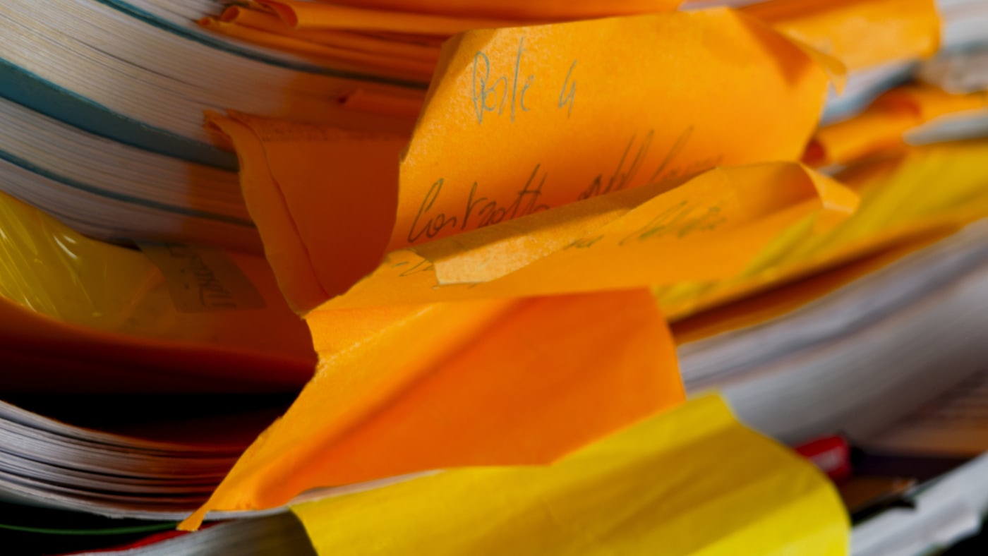 Teanc dezordonat de dosare, cu semne colorate și notițe scrise de mână ieșind dintre file.